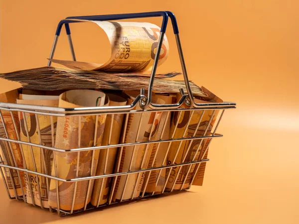 Shopping cart full of money. A shopping cart filled with euro banknotes. Shopping basket with money on an orange background.