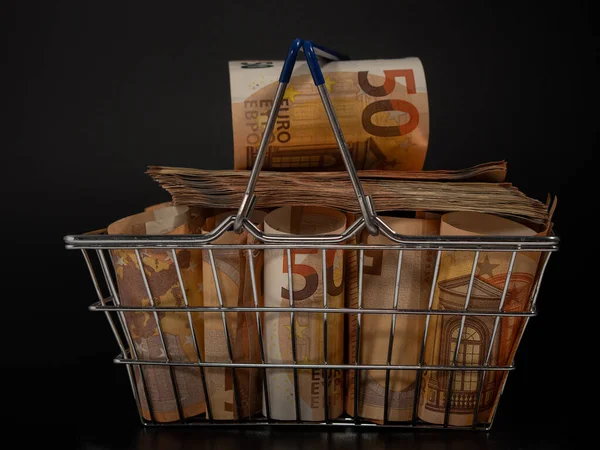 Shopping cart full of money. A shopping cart filled with euro banknotes. Shopping basket with money on a black background.