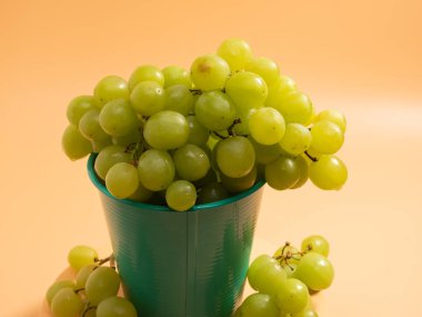 Green grapes in a bucket. Ripe grapes on an orange background. Close-up.