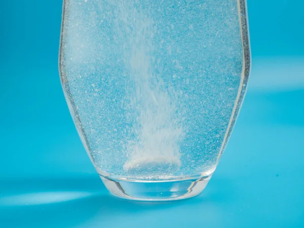 Effervescent tablet in a glass of water close-up on a blue background. Health concept.