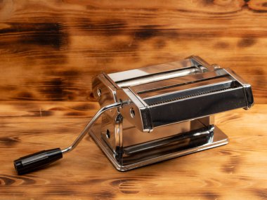Manual machine for rolling dough and pasta. Noodle cutter. Chrome plated steel. Anodized aluminium. Wooden background.