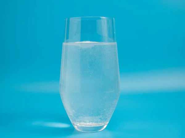 Effervescent tablet in a glass of water close-up on a blue background. Health concept.
