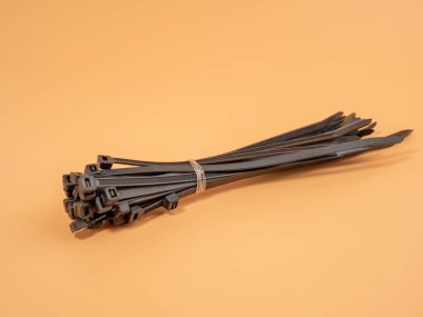 Black plastic cable ties on an orange background. Close-up.