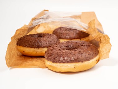 Chocolate donut with chocolate chips in a paper bag on a white background. close-up.
