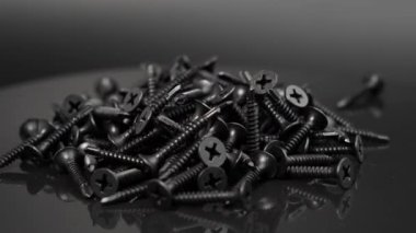 Black Screws. Rotating Black Screws for drywall on a black background. Close-up.