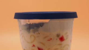 Turuncu arka planda plastik bir kavanozda vejetaryen makarna salatası. Makarna salatası..