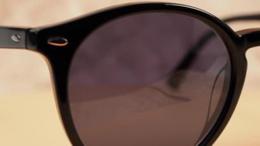 Stylish sunglasses. Dark-framed sunglasses rotate on a sandy background. Close-up.