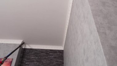 Bir kadın modern bir elektrikli süpürgeyle tavandan tozu kaldırıyor. Ev temizliği.