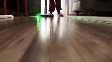 Bir kadın, modern elektrikli süpürgeyle elektrik süpürgesini yeşil ışıkla süpürüyor. Ev temizliği.
