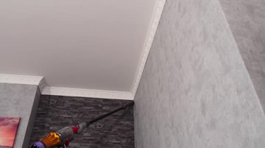 Bir kadın modern bir elektrikli süpürgeyle tavandan tozu kaldırıyor. Ev temizliği.