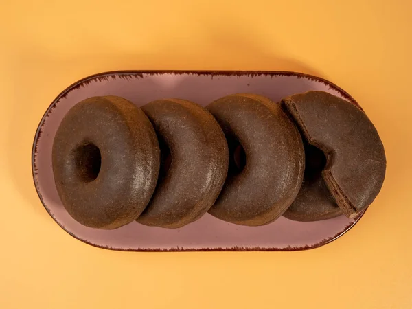 stock image Fresh dark vegetarian donut on a plate on an orange background. Close-up.