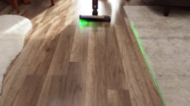 Bir kadın, modern elektrikli süpürgeyle elektrik süpürgesini yeşil ışıkla süpürüyor. Ev temizliği.