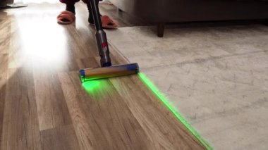 Bir kadın, modern elektrikli süpürgeyle elektrik süpürgesini yeşil ışıkla süpürüyor. Ev temizliği.