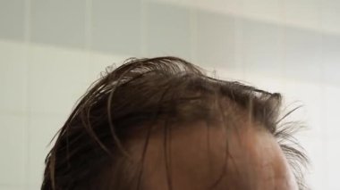 Bir adam saçını makineyle kesiyor. Evde, bir adam aynanın önünde kafasını tıraş eder. Saç dökülme problemi.