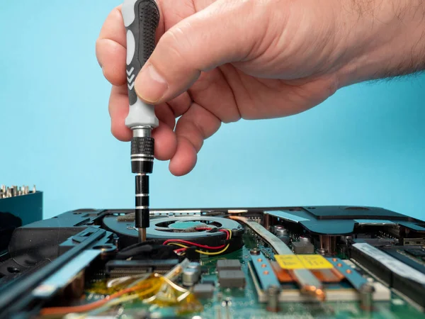The master repairs a broken laptop with a screwdriver. Specialist and old broken laptop.