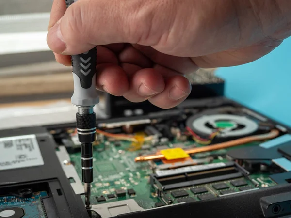 The master repairs a broken laptop with a screwdriver. Specialist and old broken laptop.