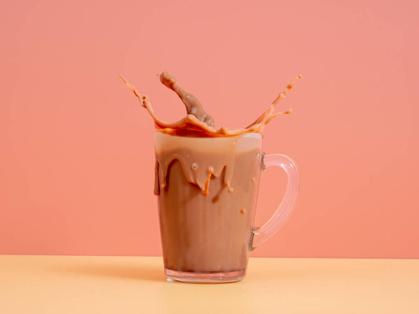 Splash of chocolate milk from a glass on a pink background. Cocoa in a glass. Splash of cocoa.