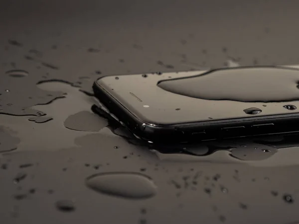 Smartphone 'un üzerine su döküldü. Akıllı telefon suya düşmüştü. Siyah arkaplanda ıslak akıllı telefon.