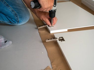 Bir adam evde profesyonel bir tornavidayla mobilya monte ediyor. Mobilya kurulumu.