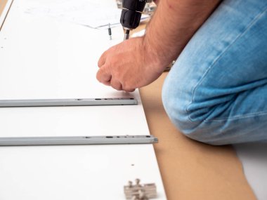 Bir adam evde profesyonel bir tornavidayla mobilya monte ediyor. Mobilya kurulumu.