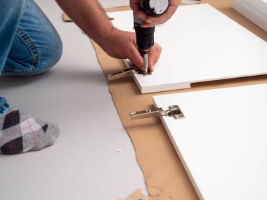 Bir adam evde profesyonel bir tornavidayla mobilya monte ediyor. Mobilya kurulumu.