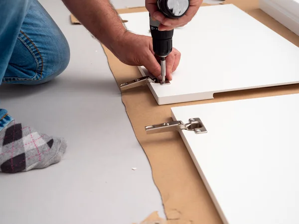 Bir adam evde profesyonel bir tornavidayla mobilya monte ediyor. Mobilya kurulumu.