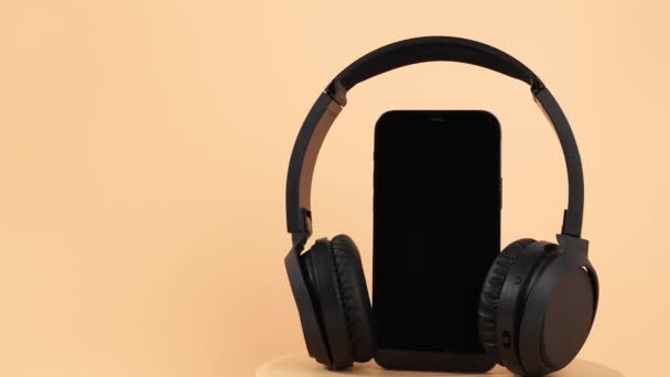 黑色无线耳机和智能手机在橙色背景下旋转 无线耳机特写 — 图库视频影像