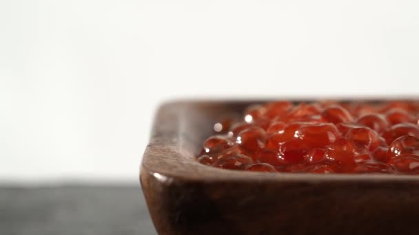 白色石板上有红色鱼子酱的木制杯子 红色鱼子酱特写在黑色背景上照相机运动 — 图库视频影像