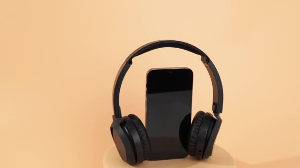 Czarne Słuchawki Bezprzewodowe Smartfon Obracają Się Pomarańczowym Tle Bezprzewodowe Słuchawki — Wideo stockowe