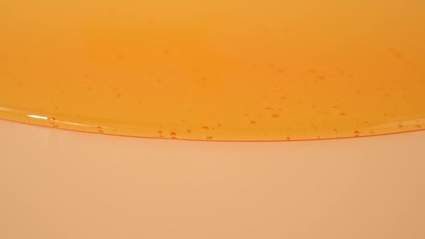 液体シャワーゲルは明るいオレンジ色の背景に優雅に流れています シャワーゲルの半透明な波は 魅惑的な視覚的な交響曲を作り出しています 液体シャワーゲルがオレンジ色の背景に流れる — ストック動画