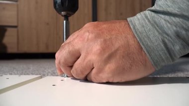 Bir usta elektrikli tornavida kullanarak mobilya monte eder. Bir adam mobilya kuruyor..