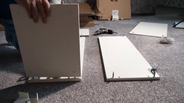 Bir usta elektrikli tornavida kullanarak mobilya monte eder. Bir adam mobilya kuruyor..