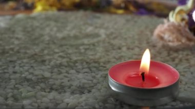 Yalnız yanan bir mum, berrak sudaki kumun üzerinde duruyor. Kumlu zeminde mumlar ve berrak su