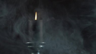 Gölgelerdeki mum ışığı. Bir şamdanın üzerine konmuş tek bir mum kadifemsi bir dumanın arasında koyu bir arkaplanda dalgalanan dumanın arasında..