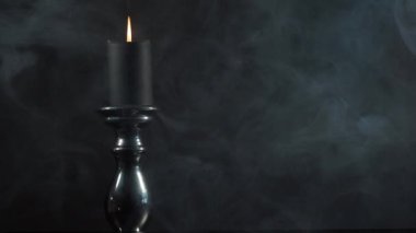 Gölgelerdeki mum ışığı. Bir şamdanın üzerine konmuş tek bir mum kadifemsi bir dumanın arasında koyu bir arkaplanda dalgalanan dumanın arasında..