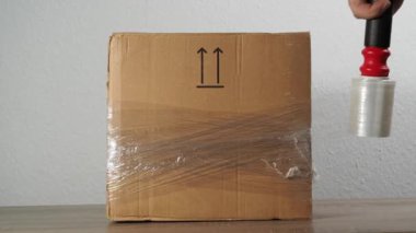 Adamın biri karton kutuyu selofanla kandırıyor. Karton kutuları paketlemek için selofan.