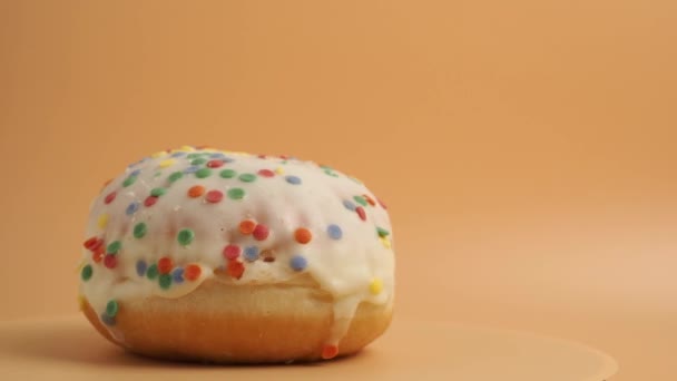 Ένα Ντόνατ Καλυμμένο Γλάσο Ζάχαρης Πολύχρωμα Ψίχουλα Περιστρέφεται Πορτοκαλί Φόντο — Αρχείο Βίντεο