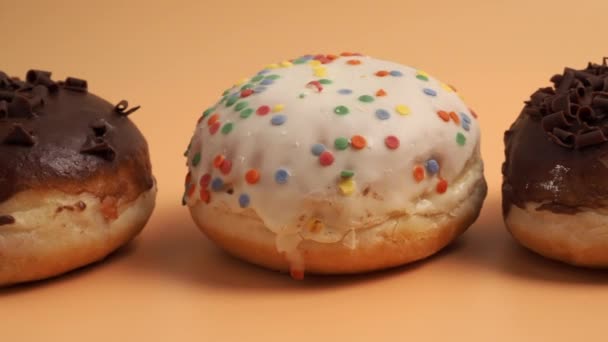 镜头在橙色背景上沿着不同口味和颜色的甜甜圈移动 甜面包特写 — 图库视频影像