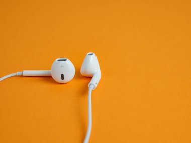 Kablolu beyaz kulaklıklar ve turuncu arka plan. Kulaklıklar yakın plan..