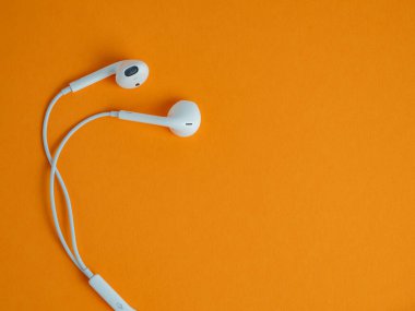 Kablolu beyaz kulaklıklar ve turuncu arka plan. Kulaklıklar yakın plan..