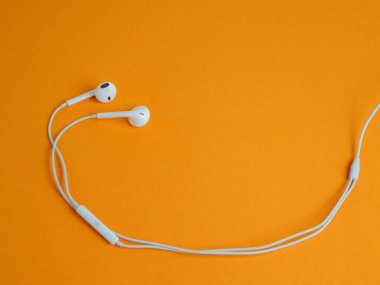 Kablolu beyaz kulaklıklar ve turuncu arka plan. Kulaklıklar yakın plan..