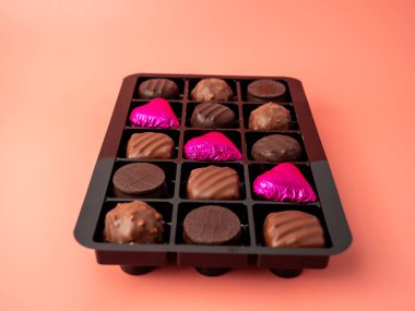 Pembe arka planda bir kutu çikolata. Çikolatalı şekerler yakın plan..