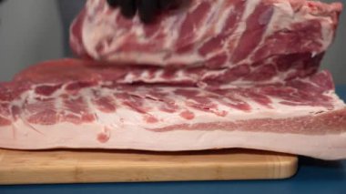 Siyah eldivenli bir adam kesme tahtasıyla domuz eti kesiyor. Domuz pişirme gösterisi.