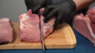 Siyah eldivenli bir adam kesme tahtasıyla domuz eti kesiyor. Yakın plan et bir profesyonel tarafından doğranıyor..