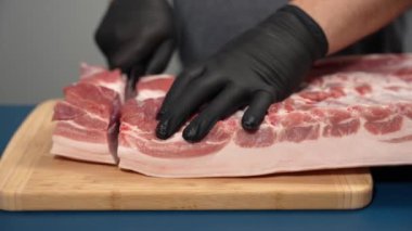 Siyah eldivenli bir adam kesme tahtasıyla domuz eti kesiyor. Domuz etini yakın plan kesiyorum..