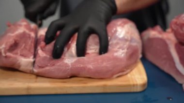 Siyah eldivenli bir adam kesme tahtasıyla domuz eti kesiyor. Deneyimli kasap domuz kesme becerisi gösteriyor...