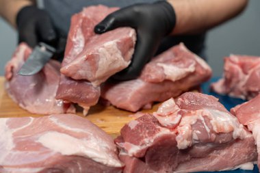 Siyah lateks eldivenli bir adam domuz etini kesme tahtasıyla keser. Domuz eti yakın plan..