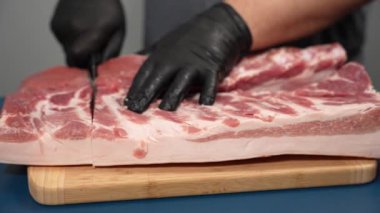 Siyah eldivenli bir adam kesme tahtasıyla domuz eti kesiyor. Domuz pişirme gösterisi.