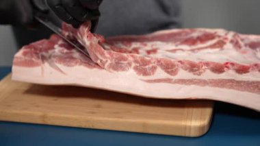 Siyah eldivenli bir adam kesme tahtasıyla domuz eti kesiyor. Domuz etini yakın plan kesiyorum..