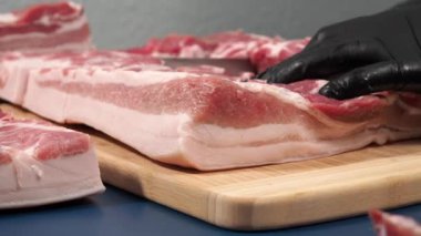 Siyah eldivenli bir adam kesme tahtasıyla domuz eti kesiyor. Domuzu zarafet ve titizlikle doğra..